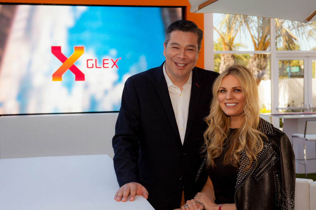 A man and woman pose together beside a presentation screen displaying the XGLEX logo.