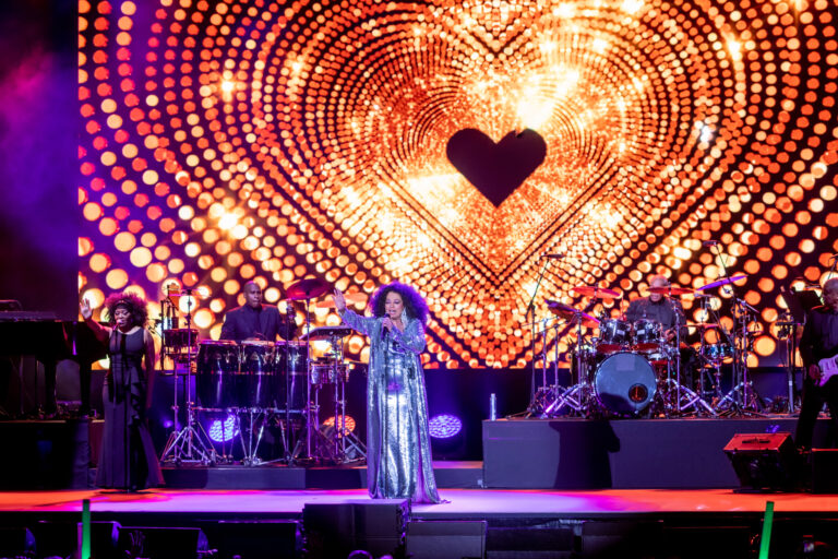A singer stands onstage beneath a large heart-shaped pattern of warm lights.