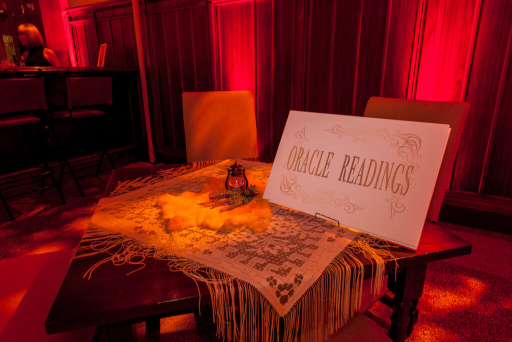 A tasseled table with a crystal ball sits beneath a sign reading Oracle Readings.