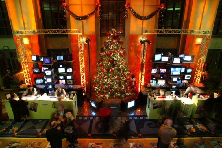Elegant corporate holiday gala ballroom with a Christmas tree, multiple TV displays and ornate architectural details, photographed in Los Angeles.