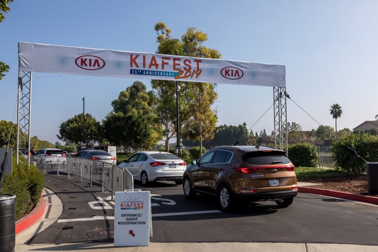 Kia Fest 25th Anniversary 2019 entrance arch with KIA logos spanning over arriving vehicles and a Guest Registration sign, photographed in Los Angeles.