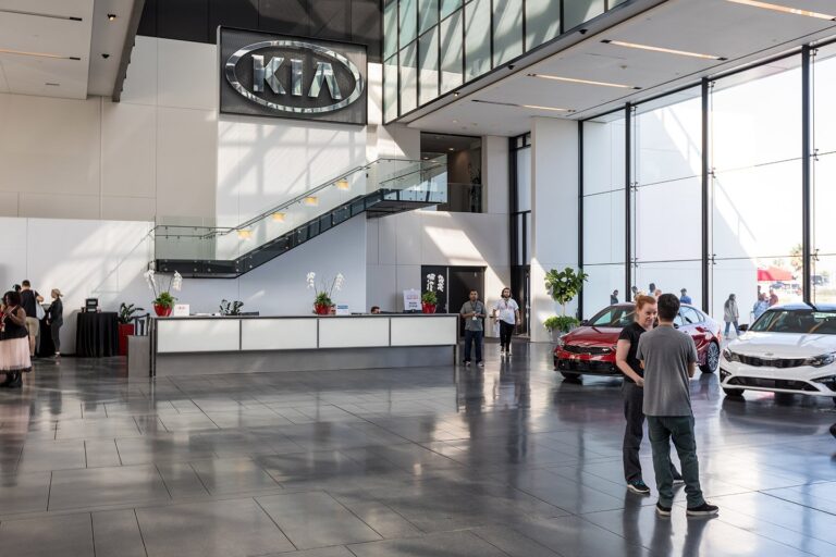 Kia America corporate showroom with the KIA logo wall, displayed vehicles and attendees networking in a modern glass-walled space, photographed in Los Angeles.