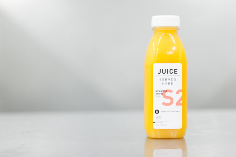 Single yellow juice bottle with a white cap photographed against a pale gray background.