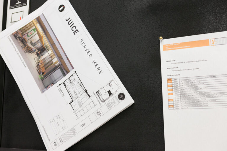 Printed juice product sheets and a bottle sample arranged diagonally on a dark surface.