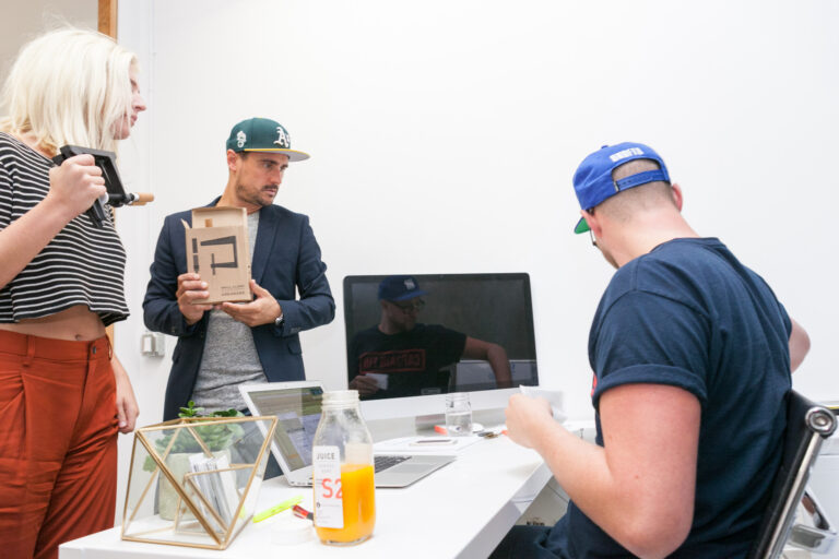 Three people review juice products and printed materials around a table in a bright workspace.