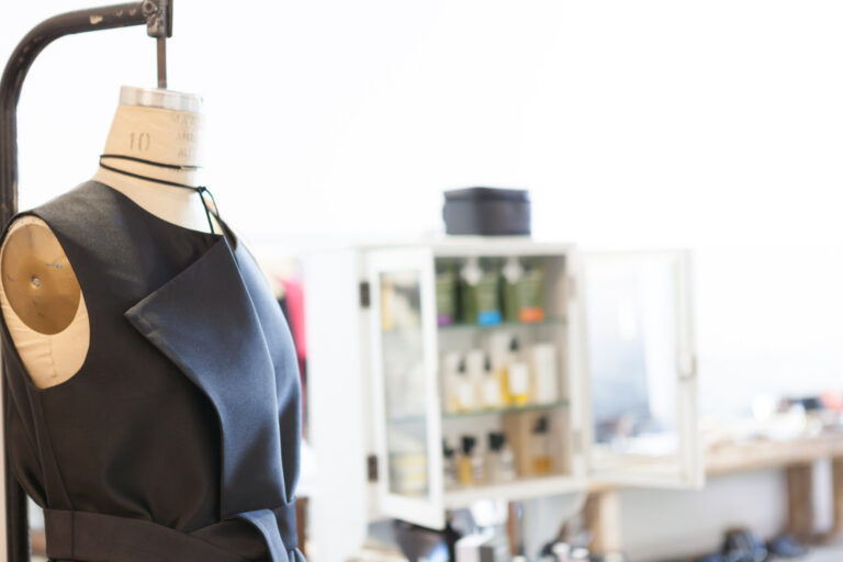 Black sleeveless garment displayed on a dress form in a bright studio or showroom.