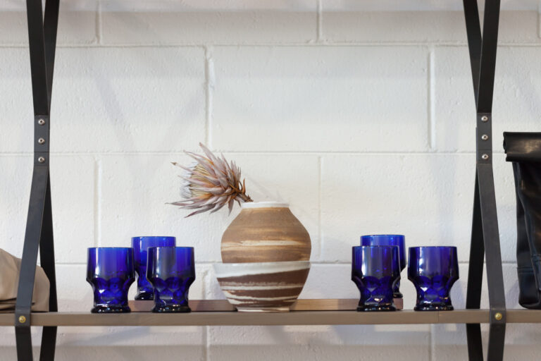 Blue glass vessels and a sculptural tan ceramic vase arranged on a shelf.