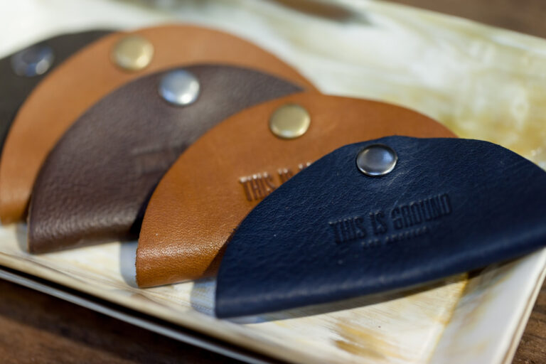 Close-up of rounded leather key fobs in navy, tan and brown with metal rivets.