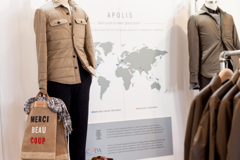 Apolis-branded display with tan and gray jackets on mannequins, a world map graphic and a “Merci Beaucoup” tote.
