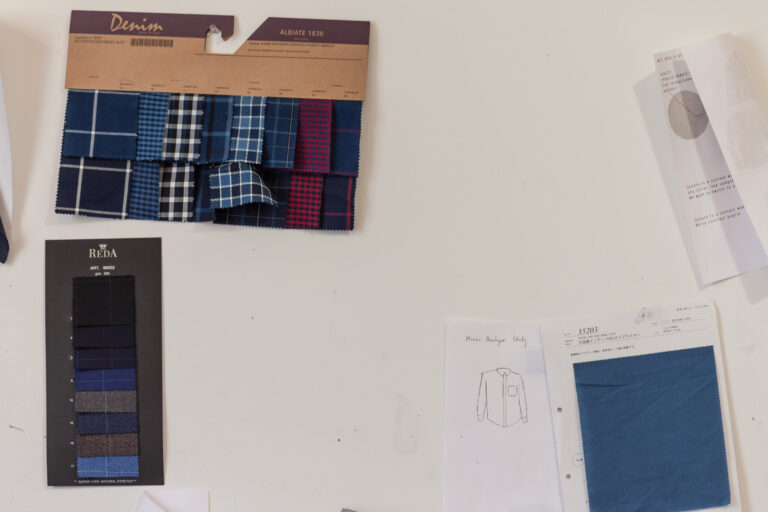 Overlapping fabric samples, a clothing sketch, measuring tape and a pen arranged on a garment-design work surface.