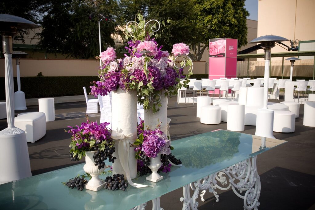 Pink and purple floral arrangements on a mirrored table at an outdoor event.