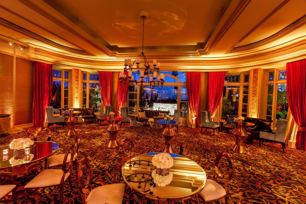 Red and gold reception room with draped ceiling, chandeliers and dining tables.